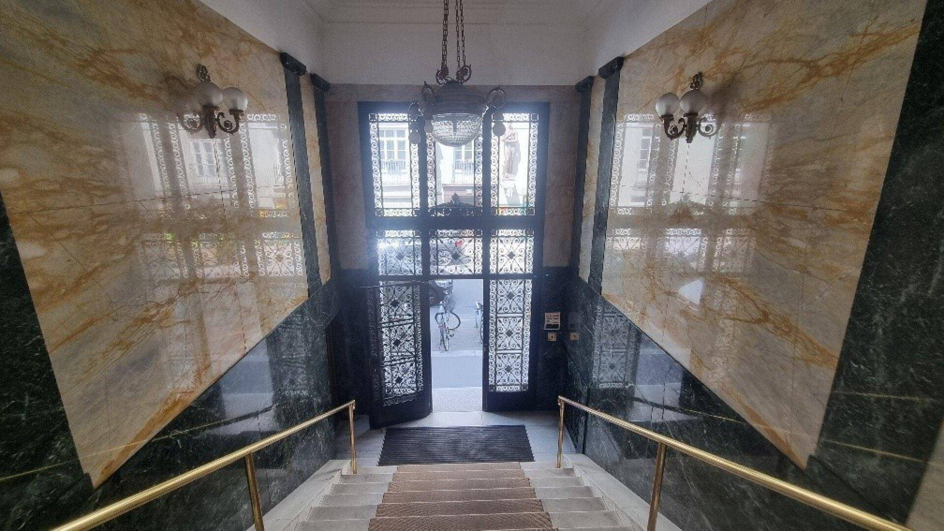 Prächtiger Eingangsbereich mit Marmorwänden, dekorativen Leuchten und einer breiten Treppe zum Gebäudeinneren.
