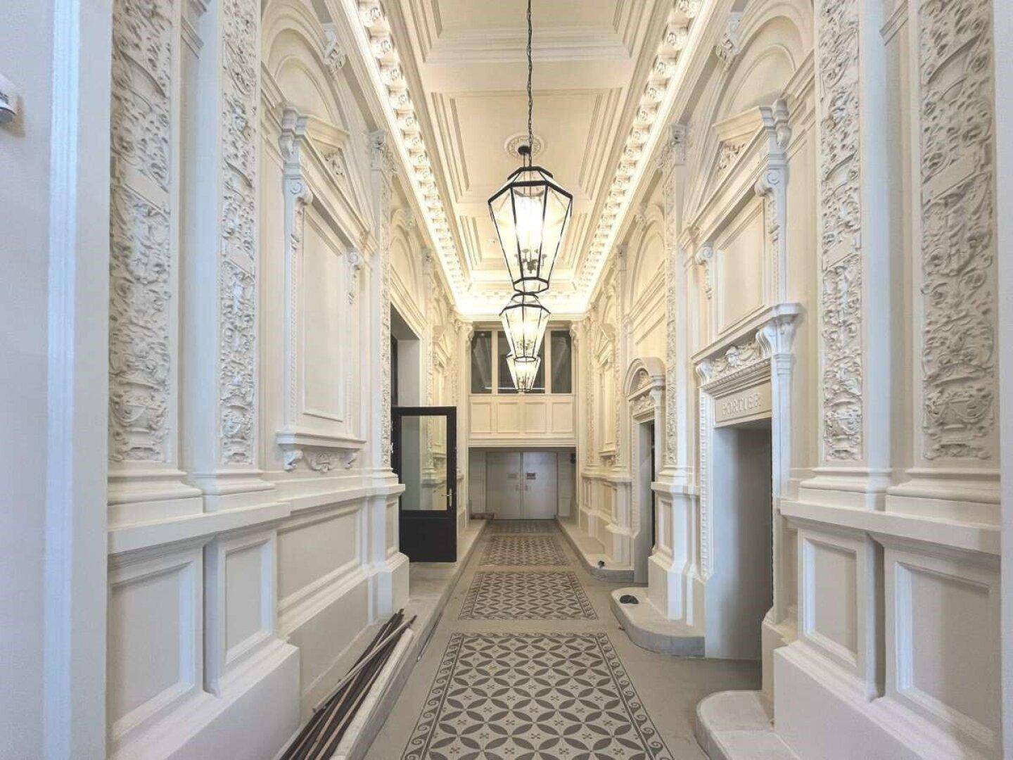 Prächtiger Eingangsbereich mit aufwendigen Stuckverzierungen, hohen Decken und eleganten Hängelampen.