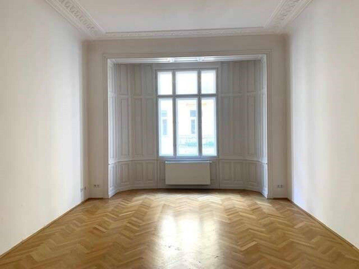 Heller Wohnraum mit Fischgrätparkett, Stuckdecke und einem charmanten Erkerfenster.