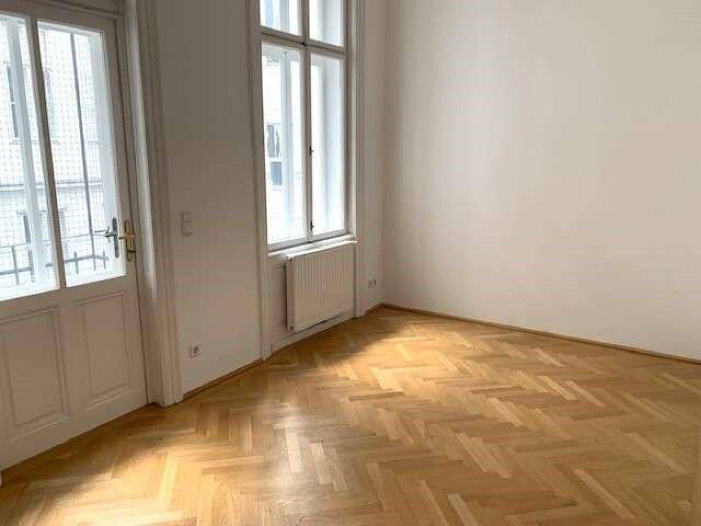 Lichtdurchfluteter Raum mit Fischgrätparkett und Zugang zu einem Außenbereich durch eine Fenstertür.
