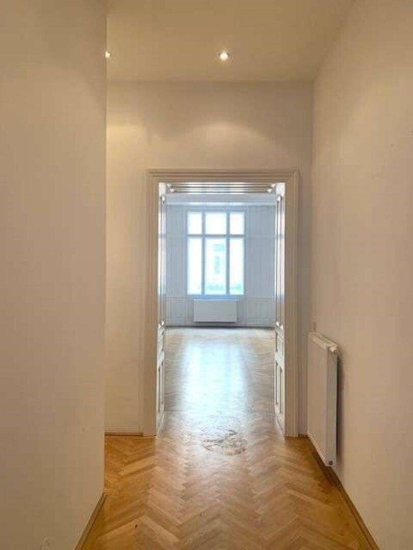 Langer Flur mit Fischgrätparkett, der in einen hellen Raum mit Erkerfenster führt.