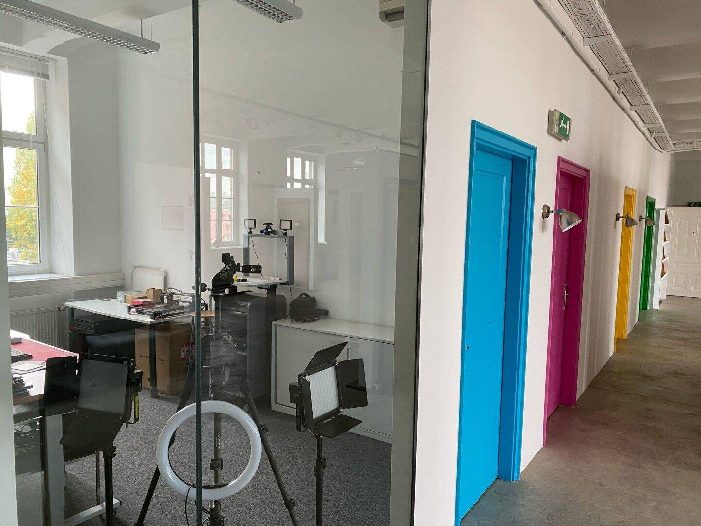Moderner Büroflur mit farbigen Türen und Glaswand, die Einblick in einen hellen Arbeitsbereich gewährt.