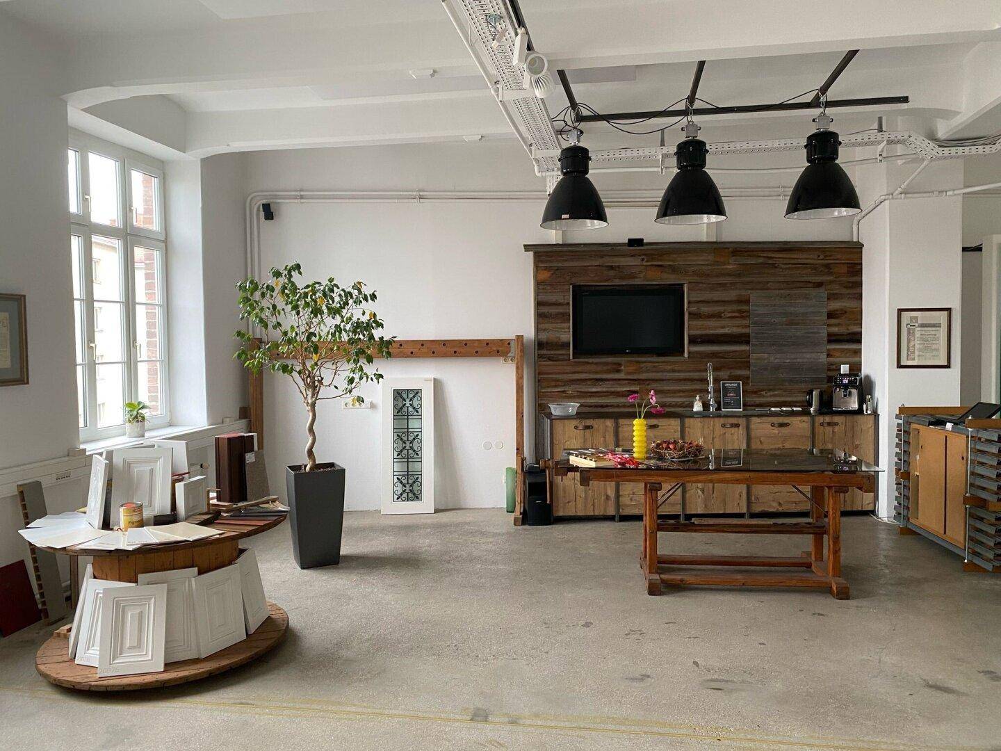 Großer, offener Studioraum mit hohen Decken, Holzwand, Kaffeestation und viel natürlichem Licht durch große Fenster.