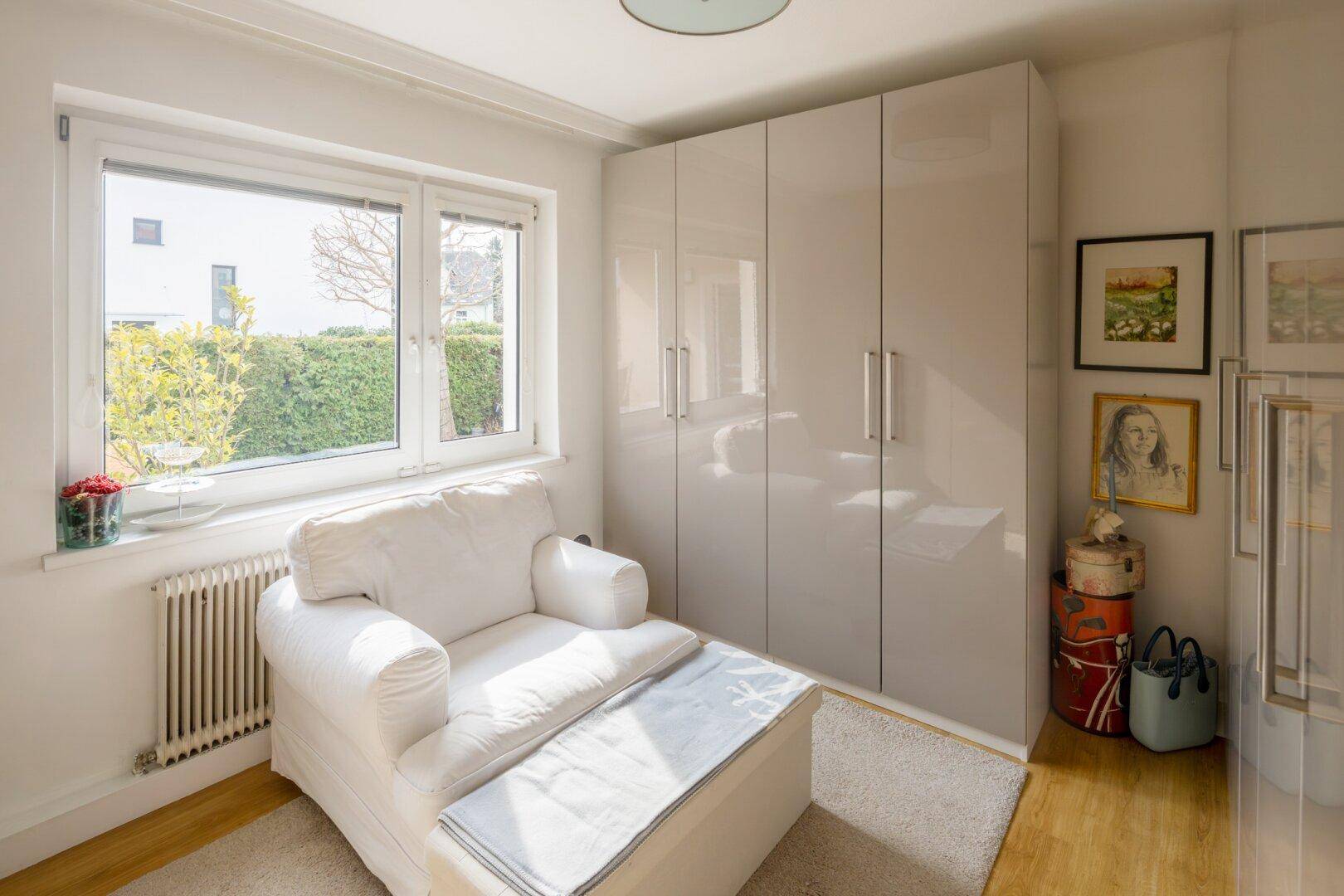 Helles Zimmer mit großem Fenster, glänzenden Einbauschränken und gemütlichem Sessel.