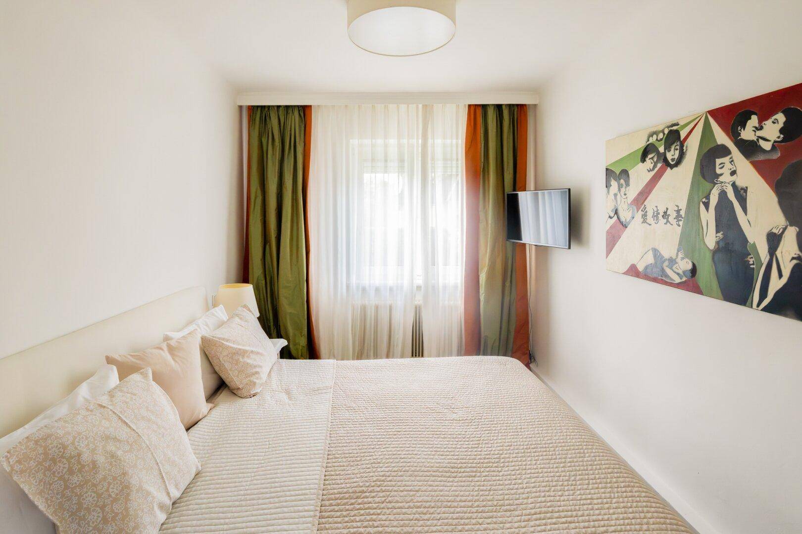 Gemütliches Schlafzimmer mit Doppelbett, modernem Kunstwerk und Blick ins Grüne.