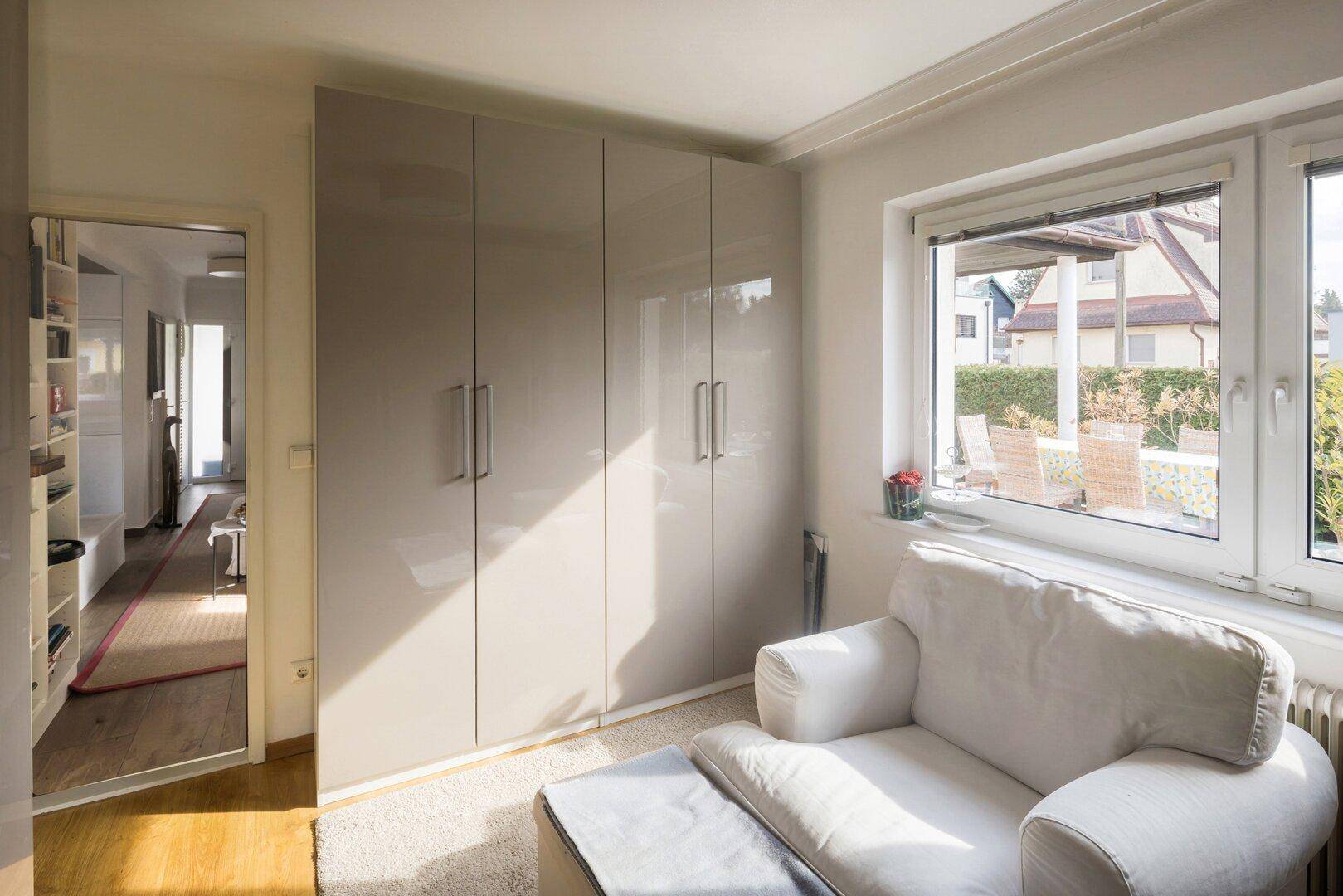 Helles Zimmer mit Einbauschränken, Sessel und Blick in den Flur.