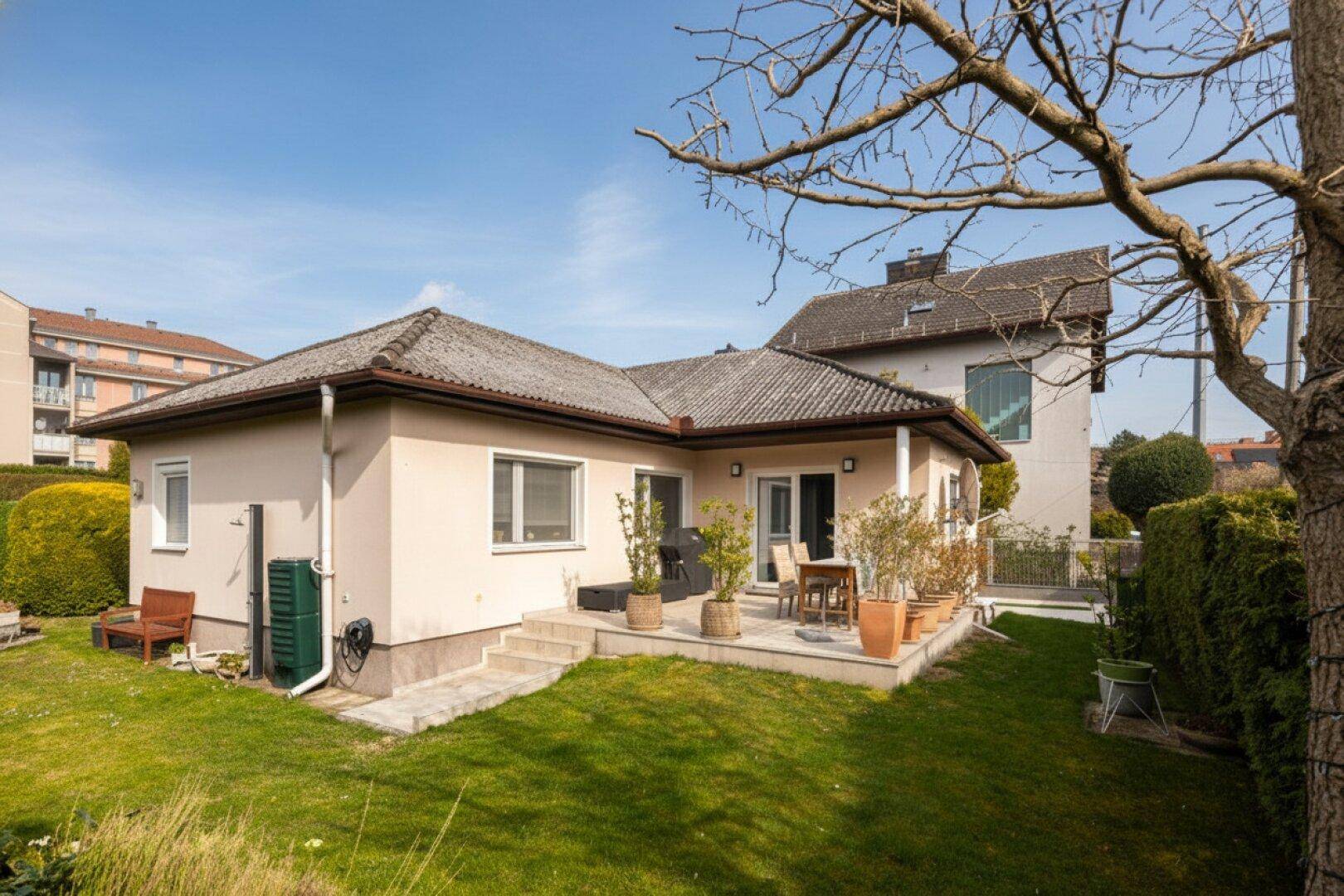 Ansicht des Hauses von der Gartenseite mit Terrasse, Rasenfläche und umliegender Bepflanzung.