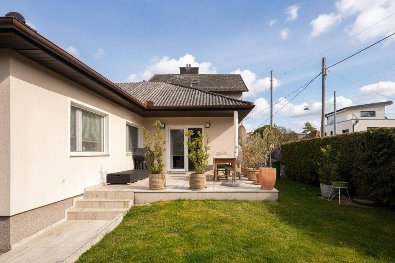 Blick auf die Terrasse vom Garten aus mit Zugang zum Haus und umliegender Grünfläche.
