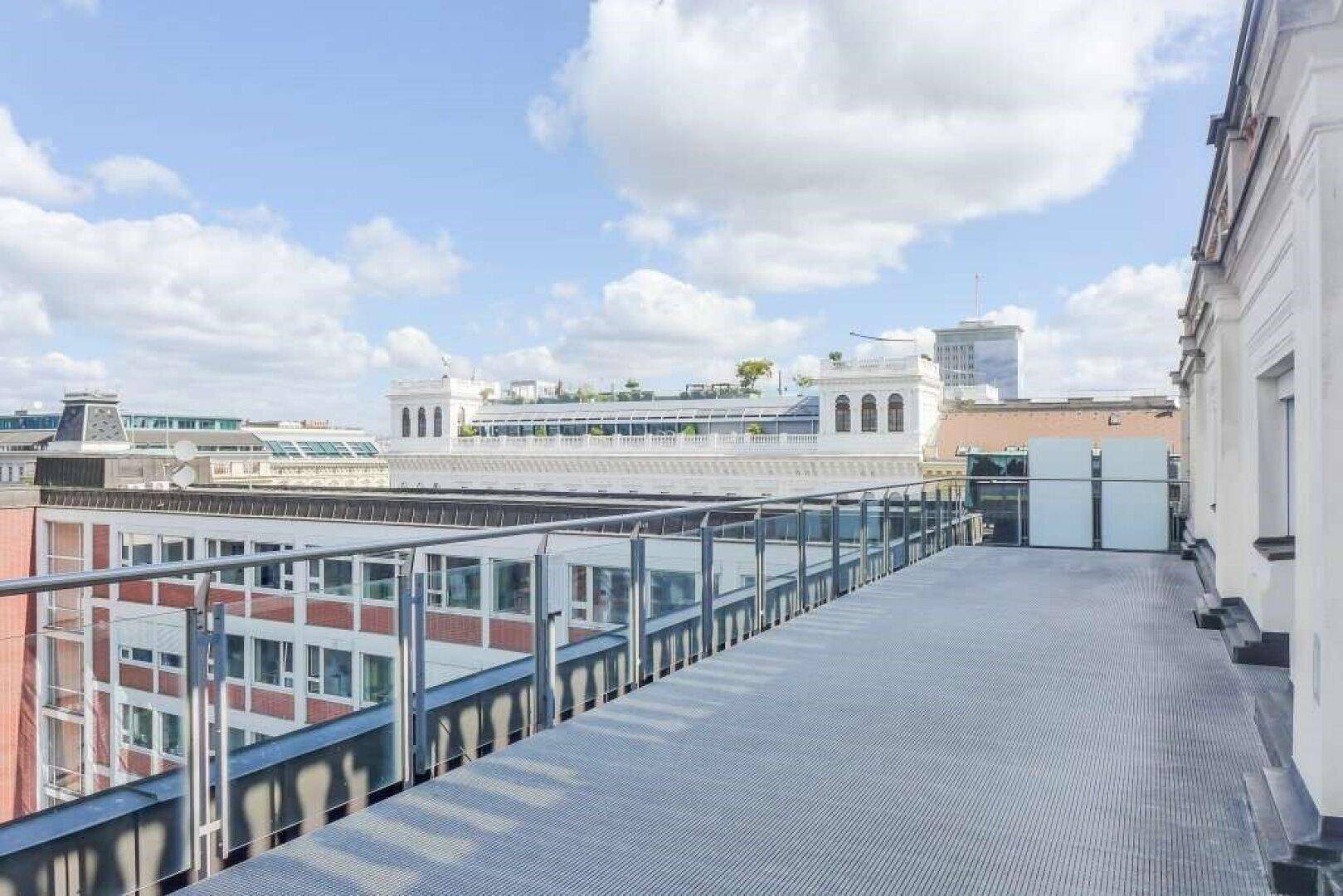 Geräumige Dachterrasse mit modernem Metallboden und Glasgeländer, bietet eine weite Aussicht über die städtische Skyline.