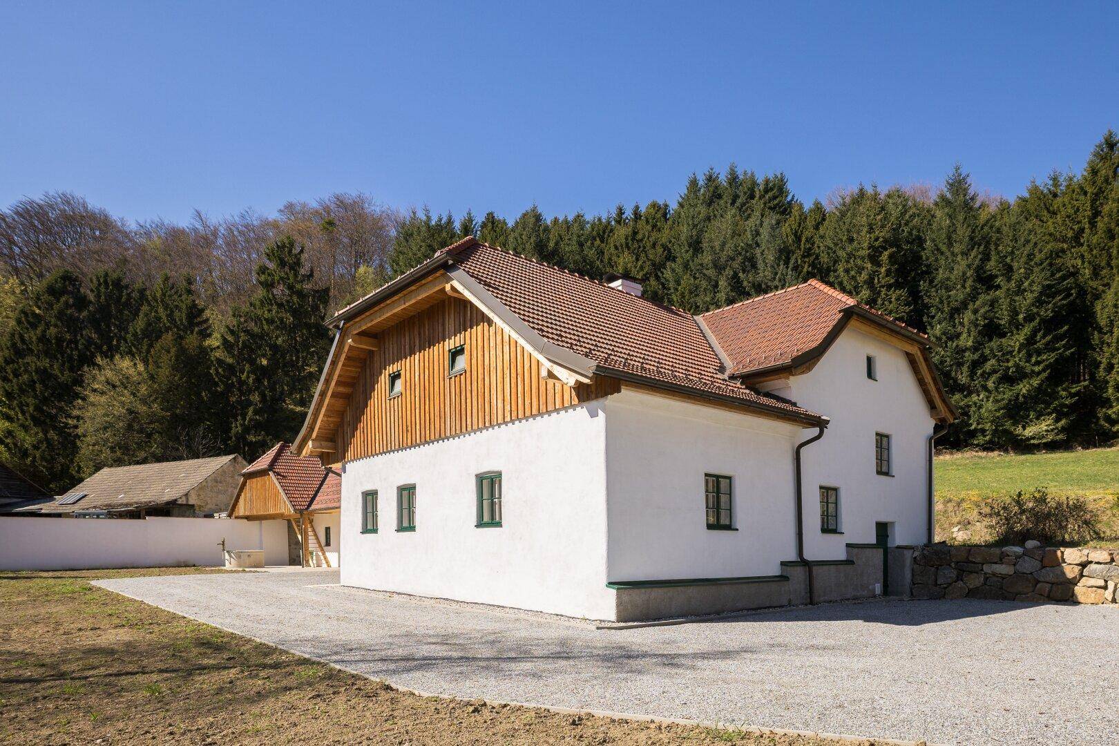 Seitenansicht des Landhauses mit weißer Fassade, Holzelementen und einem Kiesweg.