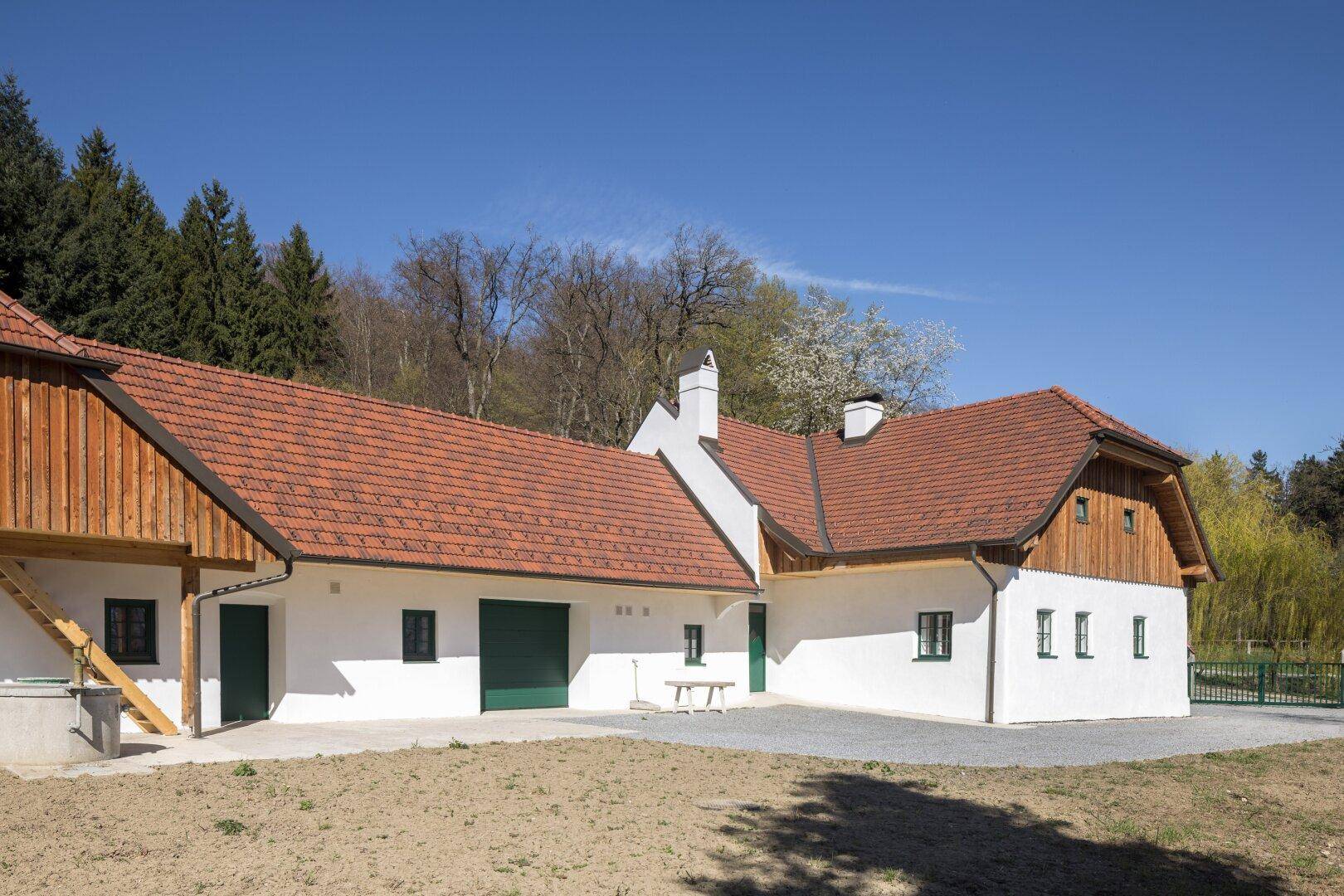 Rückansicht des Landhauses mit weißer Fassade, rotem Ziegeldach und grünen Garagentoren.