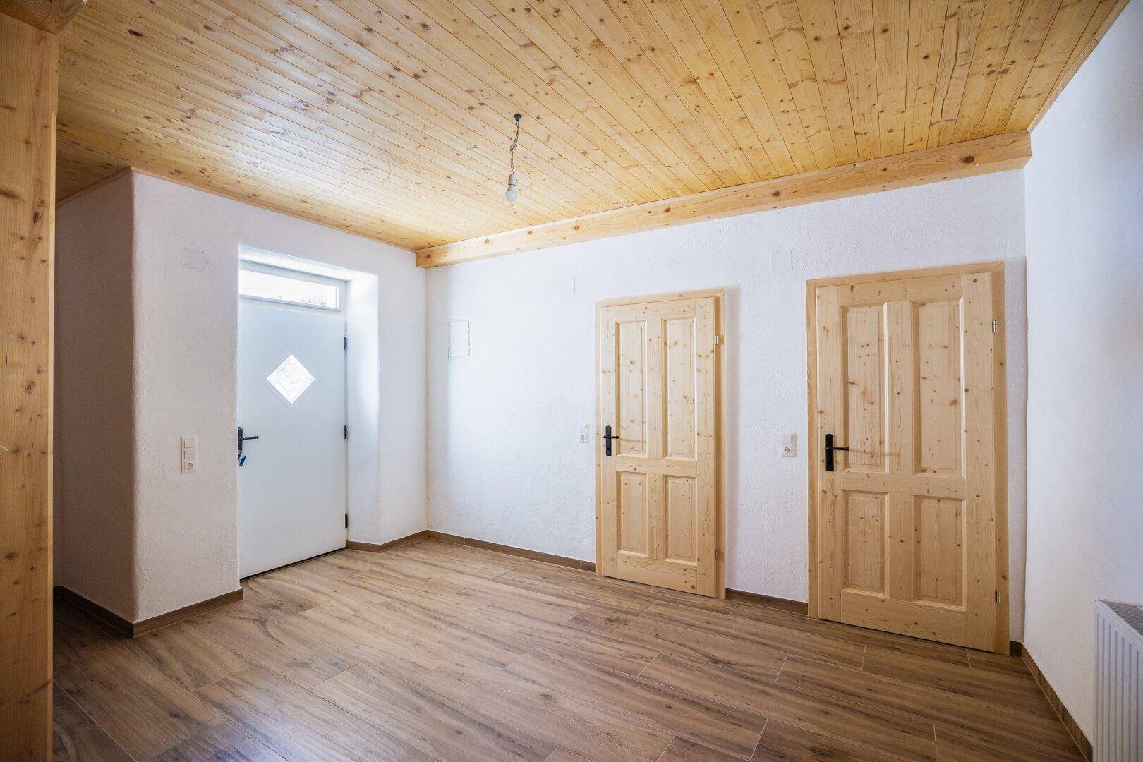 Geräumiger Flur mit Holztüren, Holzdecke und Fliesenboden, hell und einladend.