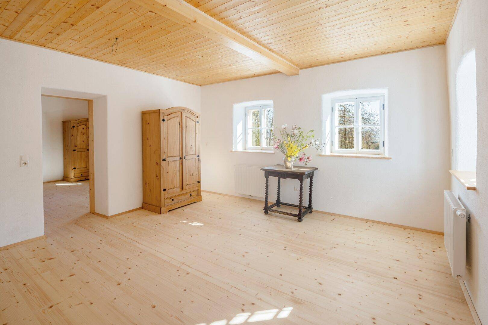 Geräumiges Schlafzimmer mit hellem Holzfußboden, zwei Fenstern und einem traditionellen Holzschrank.