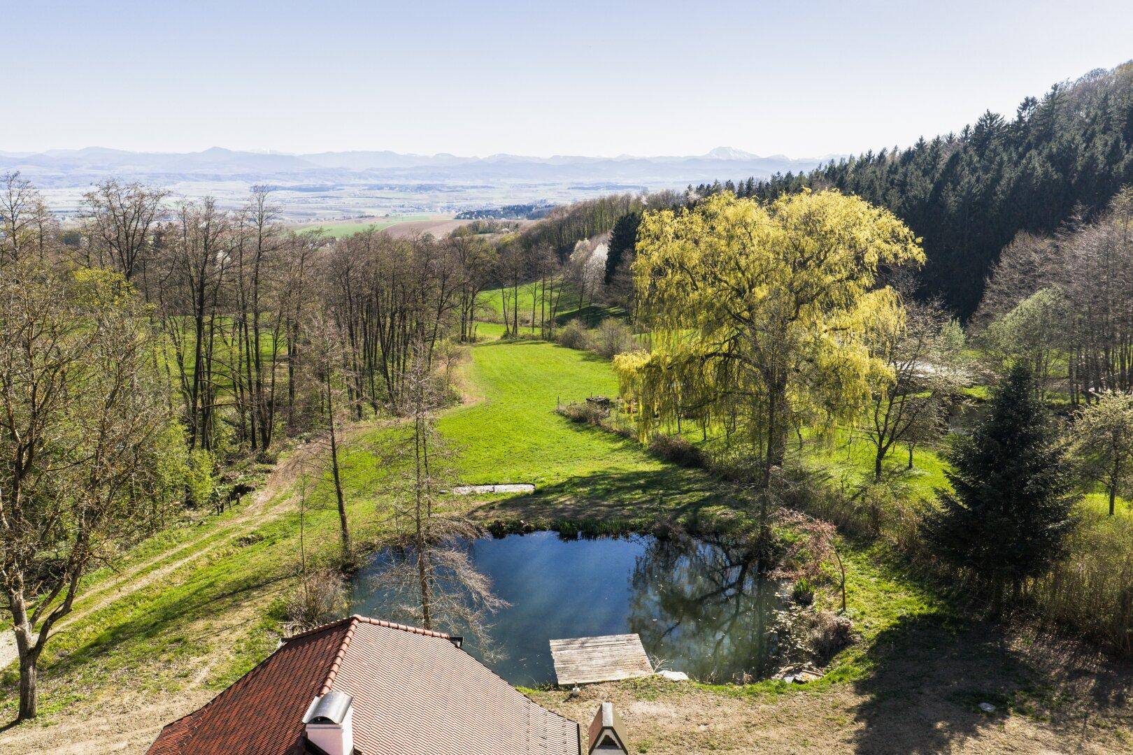 Panoramablick aus der Vogelperspektive auf das Anwesen mit Teich und weitem Blick auf die Landschaft und Berge.
