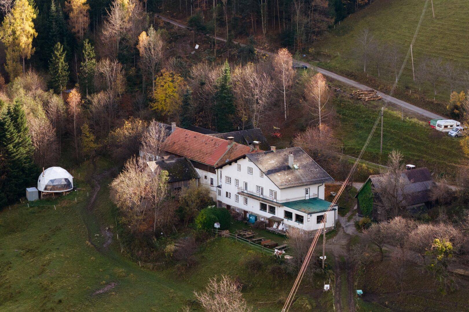Luftaufnahme des Anwesens mit angrenzendem Wald und einer kleinen Kuppelstruktur.