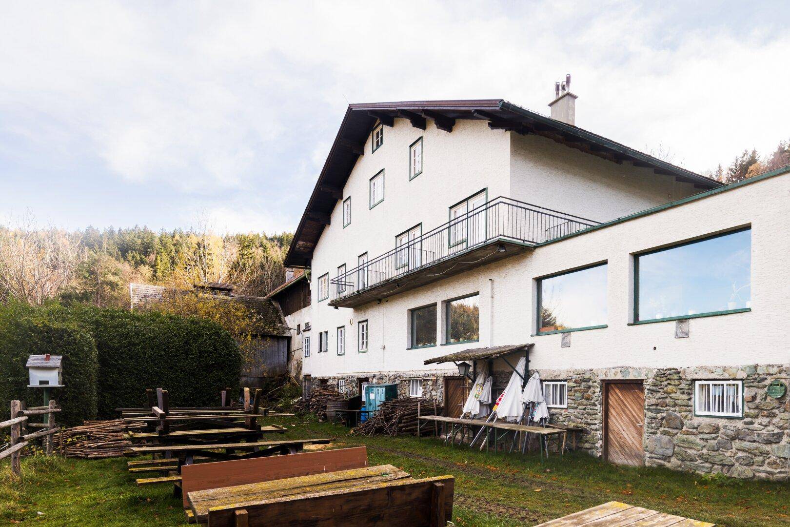 Seitenansicht des Gebäudes mit rustikalen Holzbänken und Tischen im Außenbereich.