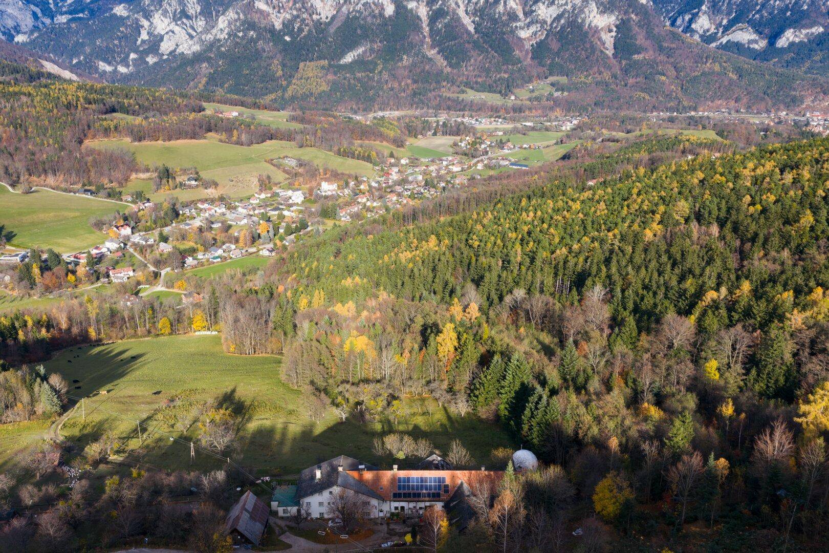 Weitläufige Luftaufnahme des Anwesens mit umliegenden Wäldern und einem Dorf im Tal.