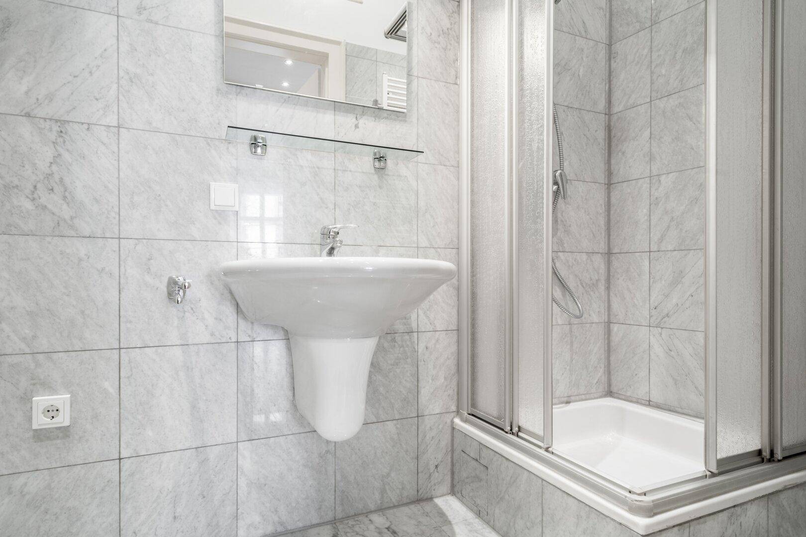 Helles Badezimmer mit grauen Fliesen, einer Duschkabine und einem modernen Waschbecken.