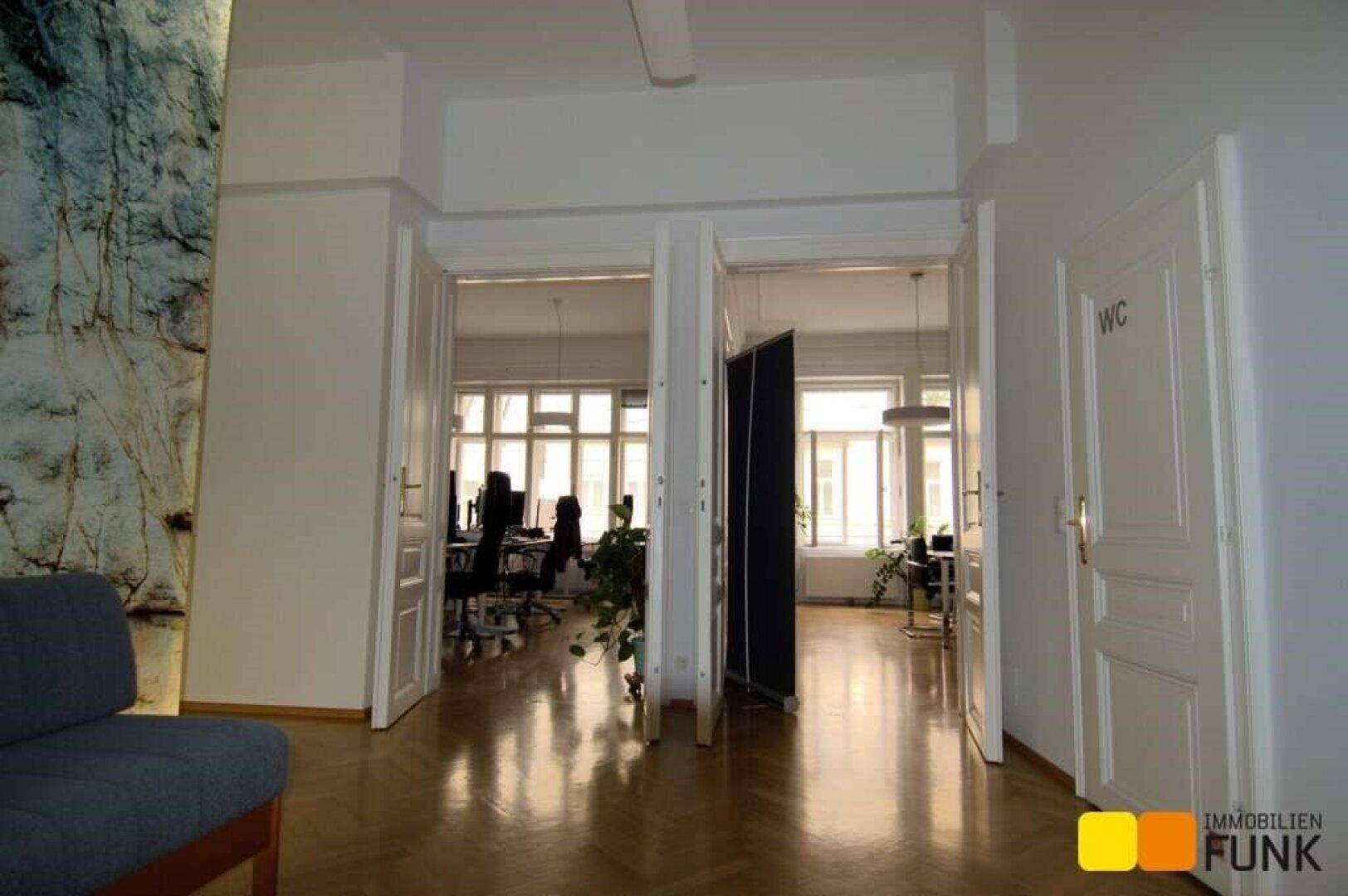 Heller Flur mit Fischgrätparkett, der zu weiteren Büroräumen und einer Toilette führt.