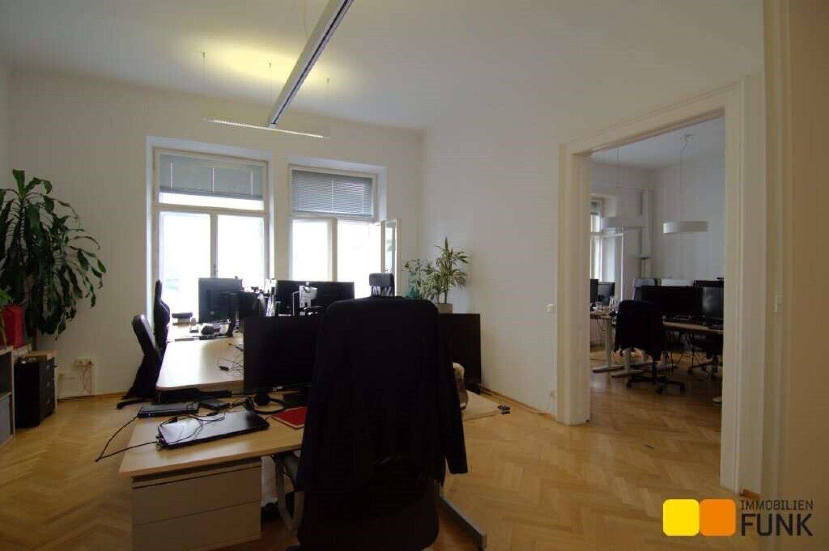 Großraumbüro mit mehreren Arbeitsplätzen, großen Fenstern und klassischem Fischgrätparkettboden.