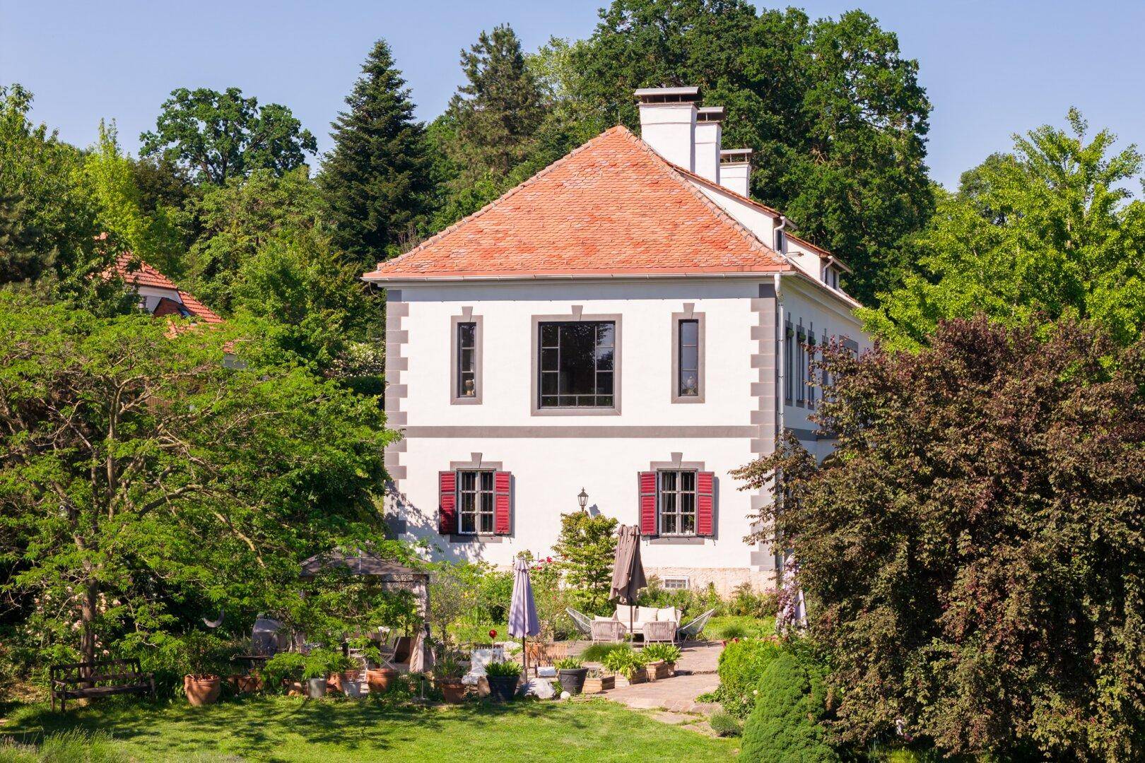 Seitenansicht der Villa mit roten Fensterläden und weitläufigem Gartenbereich.