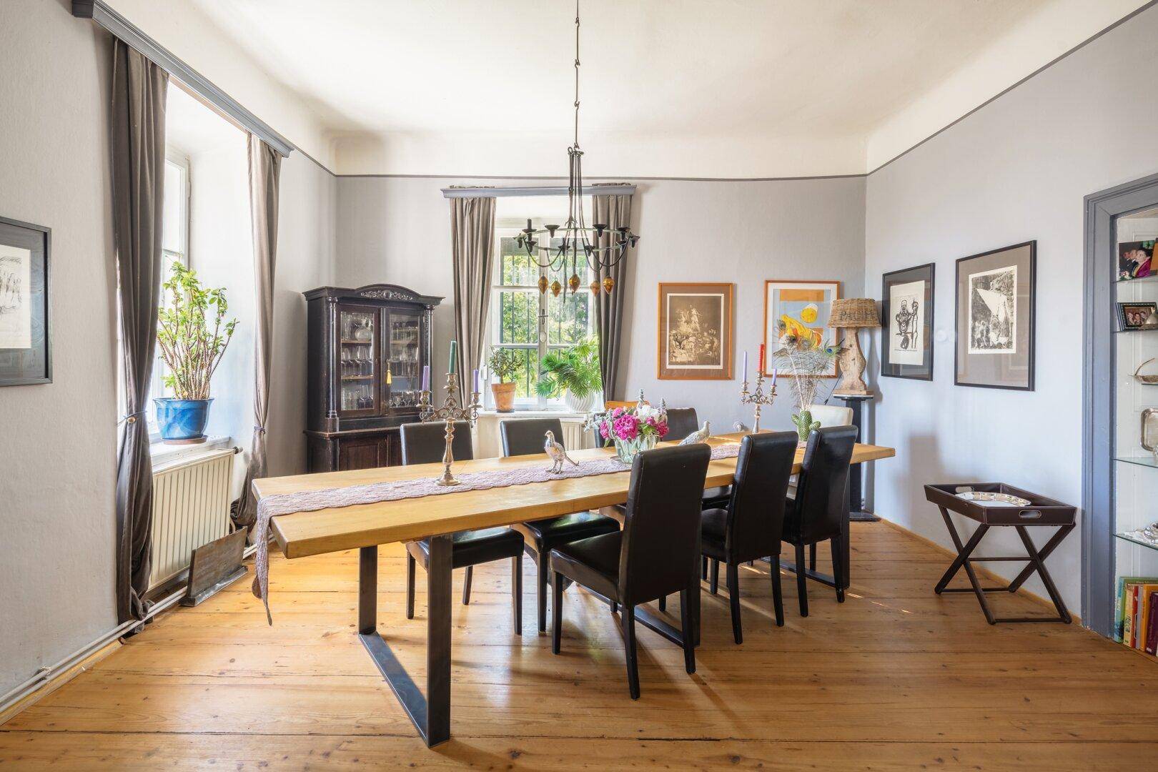 Eleganter Essbereich mit großem Holztisch, Kronleuchter und Blick in den Garten.