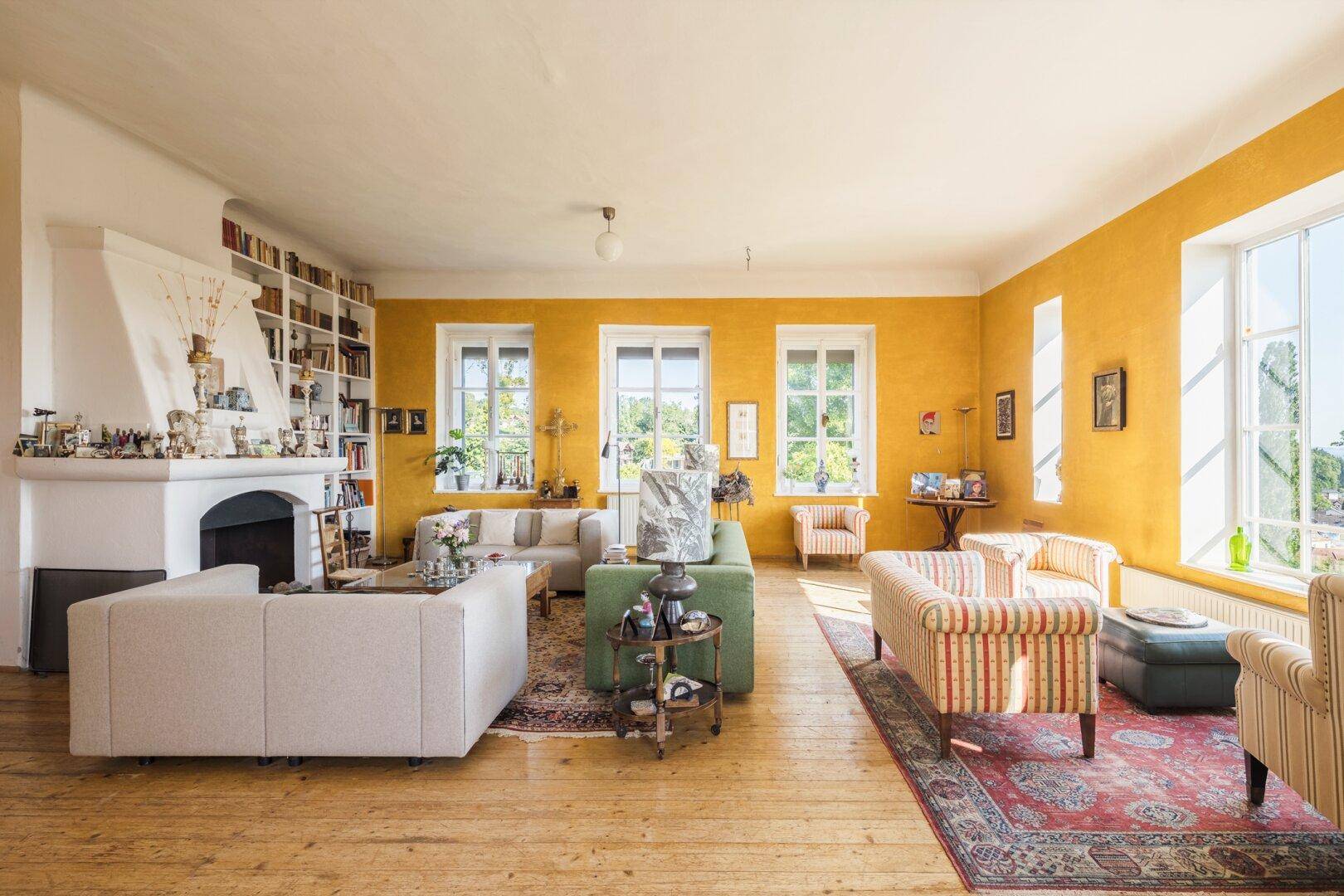 Helles Wohnzimmer mit gelben Wänden, Kamin und Holzboden, reich an Büchern und Kunst.