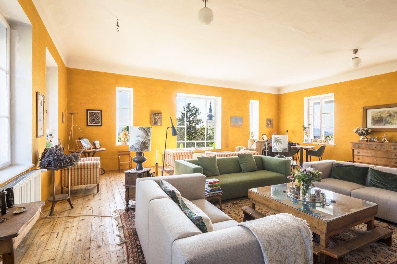 Geräumiges Wohnzimmer mit mehreren Sitzbereichen, Holzboden und Blick auf die Umgebung.