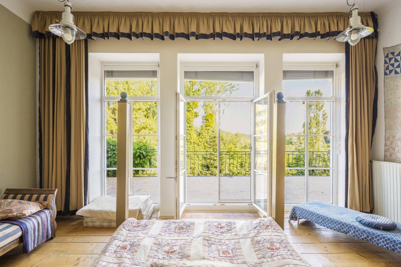 Schlafzimmer mit Holzboden und Zugang zu einem Balkon, der einen Blick ins Grüne bietet.