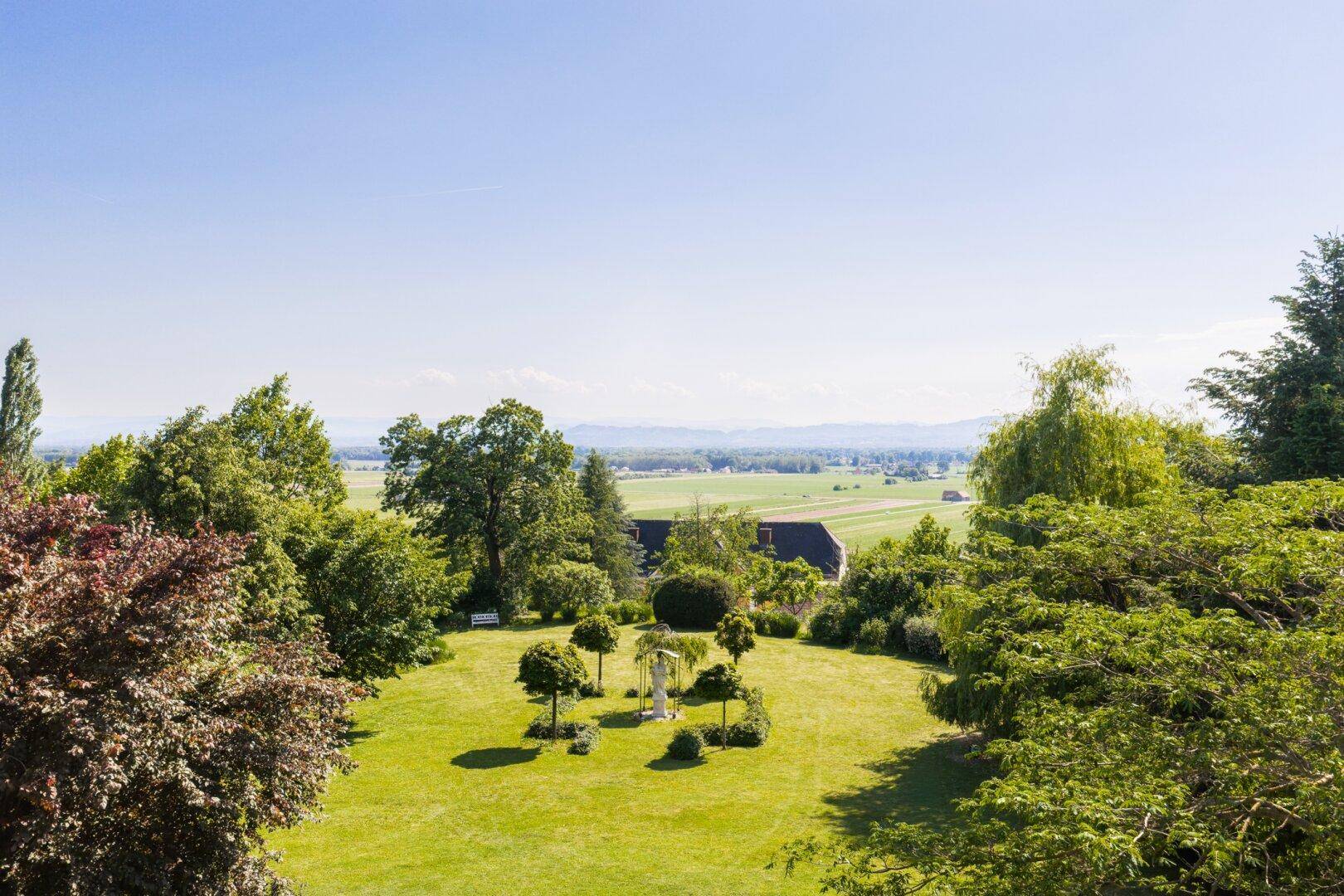 Weitläufiger Garten mit gepflegtem Rasen, Zierbäumen und Fernblick über die Landschaft.