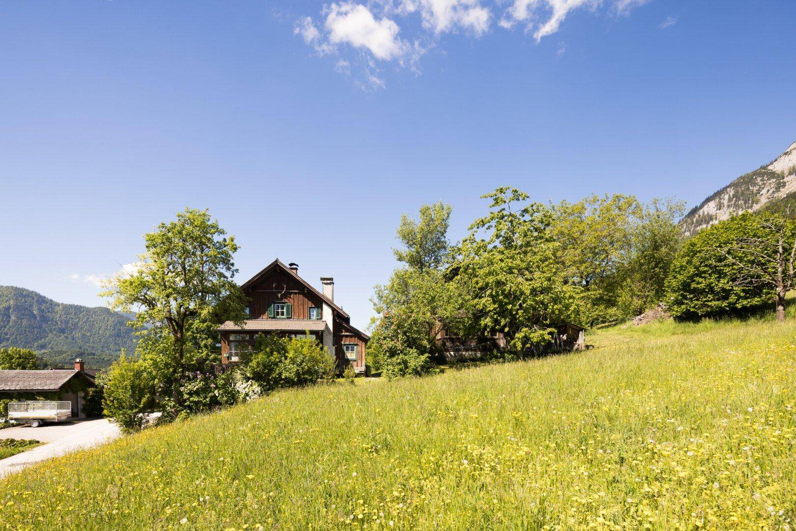 Traditionelles Holzhaus mit weitläufigem Garten und Blick auf die umliegende Berglandschaft.