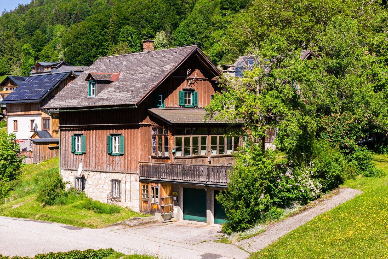 Traditionelles Holzhaus mit Balkon, grünen Fensterläden und Solarpaneelen auf dem Dach.
