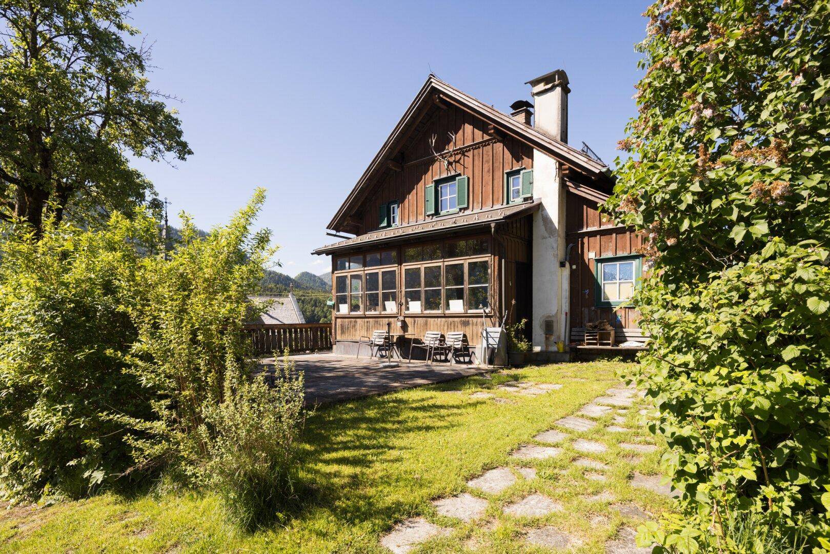Sonniger Terrassenbereich vor dem Holzhaus mit Gartenmöbeln und Blick ins Grüne.