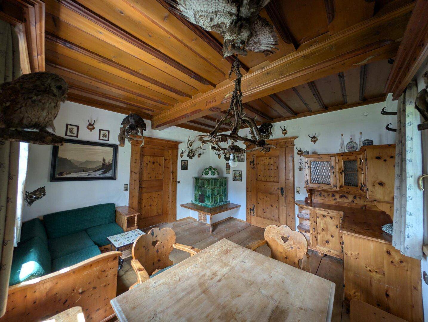 Gemütlicher Wohnbereich im alpinen Stil mit Holzbalken, Kachelofen und traditionellen Möbeln.
