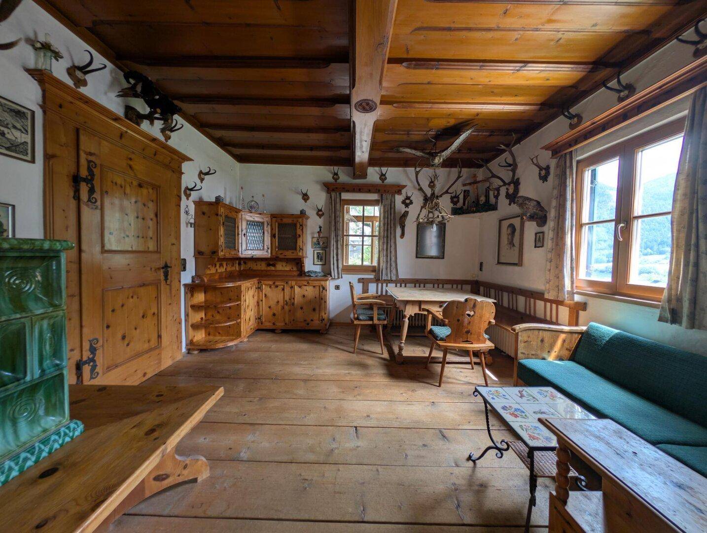 Rustikaler Wohn- und Essbereich mit Holzbalkendecke, Dielenboden und traditionellem Kachelofen.