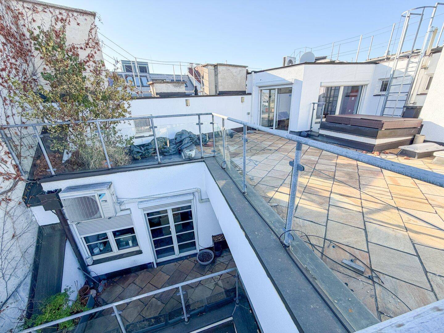 Dachterrasse mit Glasgeländer, Fliesenboden und Blick auf die umliegende Stadt und Natur.