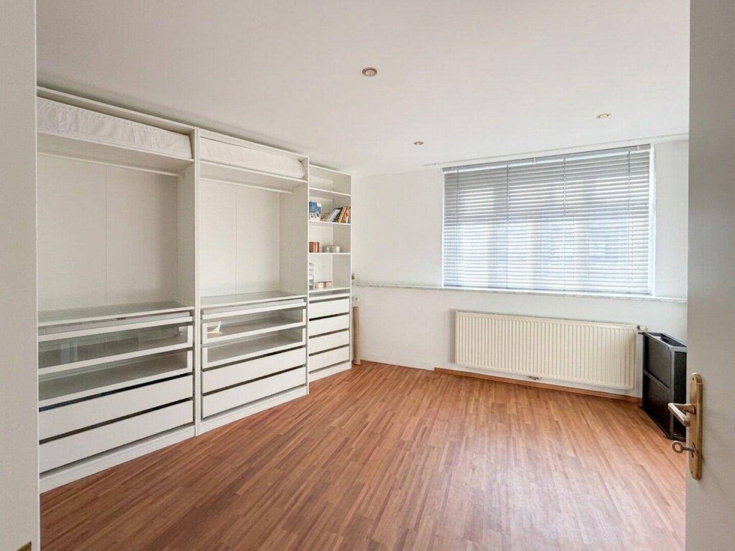 Schlafzimmer mit Einbauschränken, Holzboden und Fenster mit Jalousien für Privatsphäre.