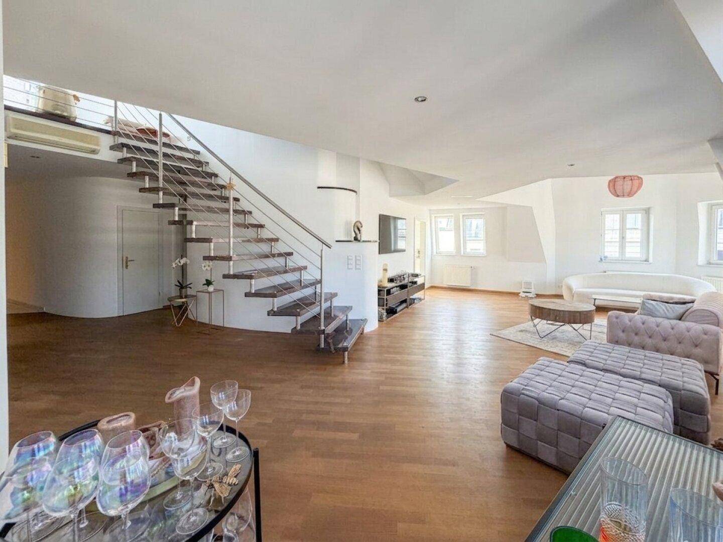Offener Wohnbereich mit eleganter Treppe, Holzboden und viel Tageslicht, das den Raum erhellt.