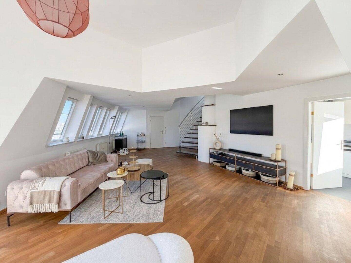 Geräumiges Wohnzimmer mit Holzboden, Dachschrägen und Zugang zu weiteren Räumen der Wohnung.