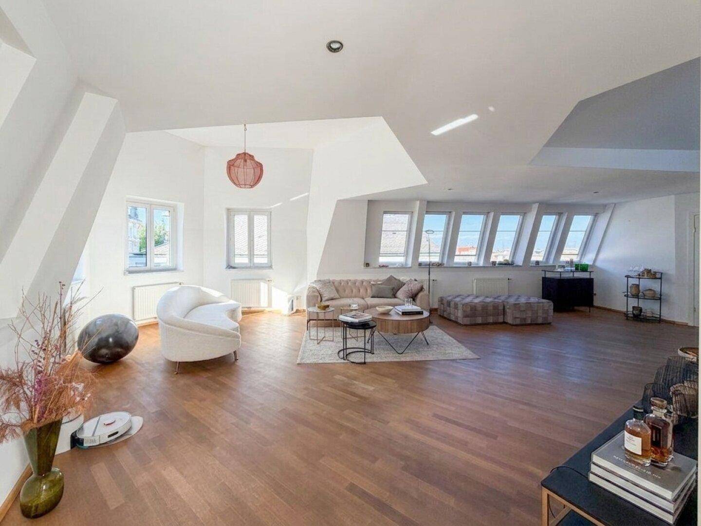 Großzügiges Wohnzimmer mit Holzboden, vielen Fenstern und moderner Dekoration, die den Raum belebt.