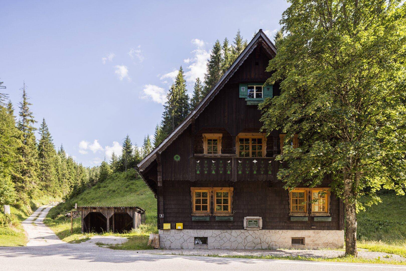 Traditionelles Holzhaus mit Satteldach und Holzbalkon, umgeben von alpiner Natur.