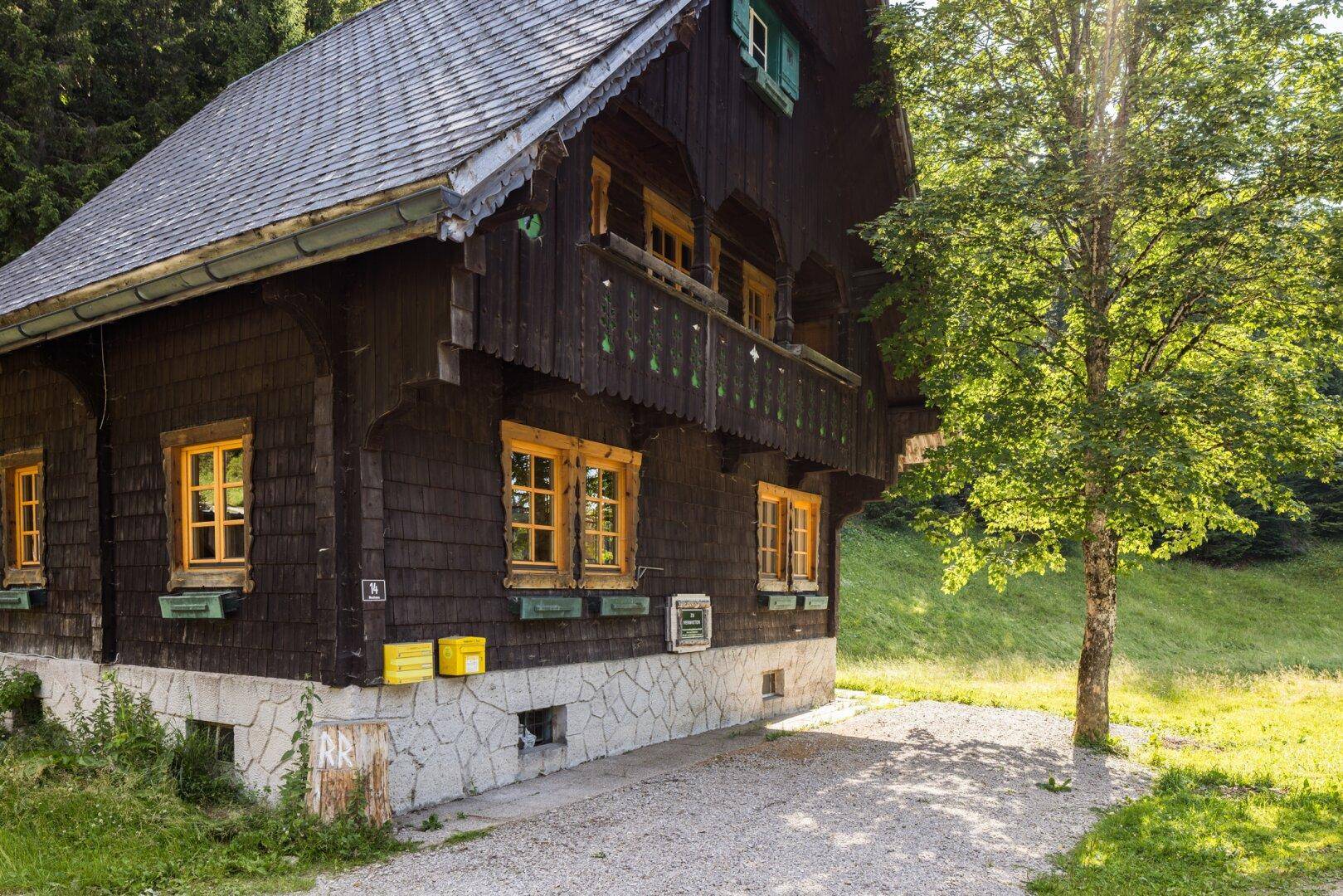 Rustikales Holzhaus mit Steinsockel und traditionellen Fensterläden in sonniger Lage.