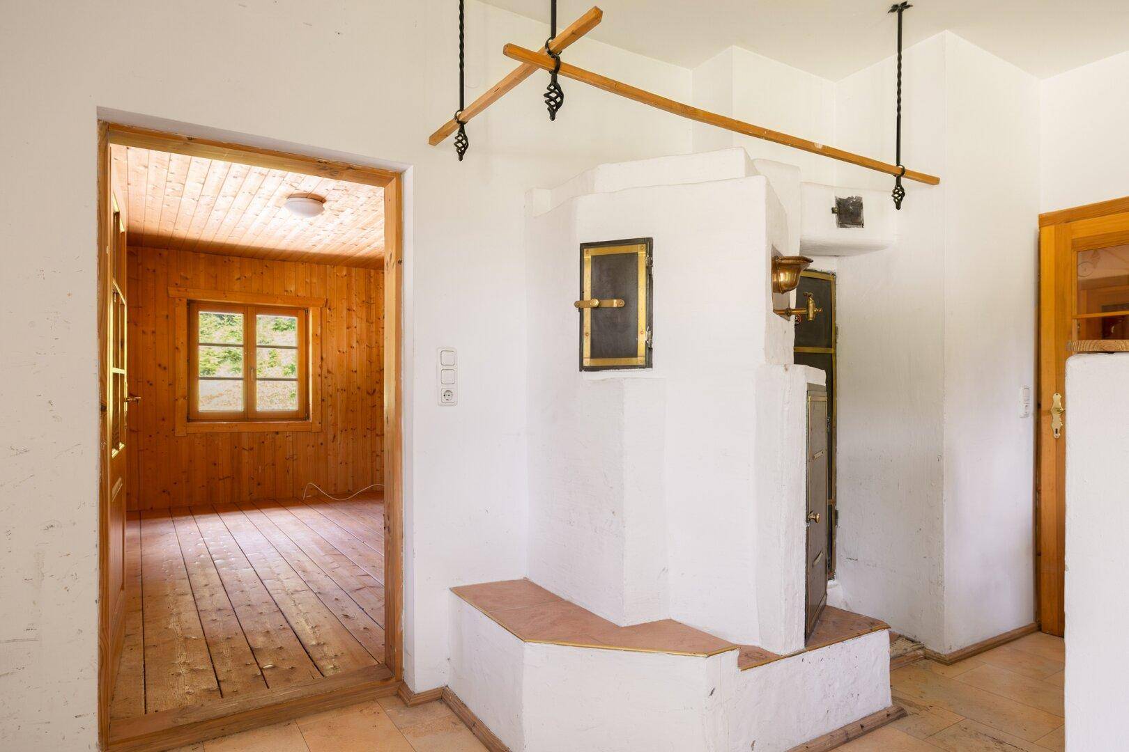 Detailansicht eines traditionellen Kachelofens in einem Raum mit Holztür und Blick nach draußen.