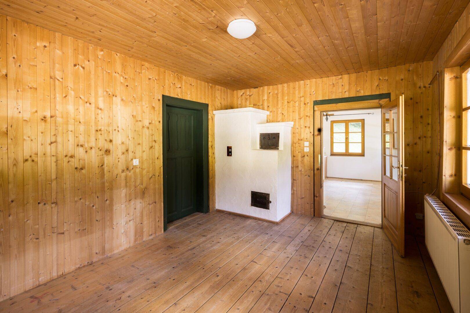 Wohnraum mit Holztäfelung, Holzdielenboden und einem traditionellen Kachelofen.