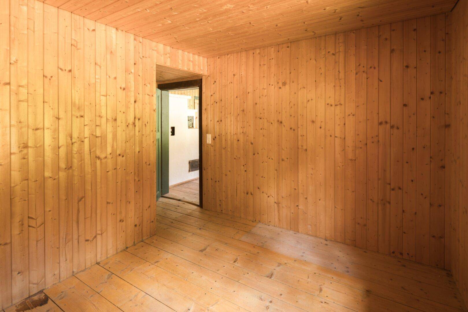 Einfaches Zimmer mit durchgehender Holztäfelung und Holzdielenboden, ideal für Renovierung.