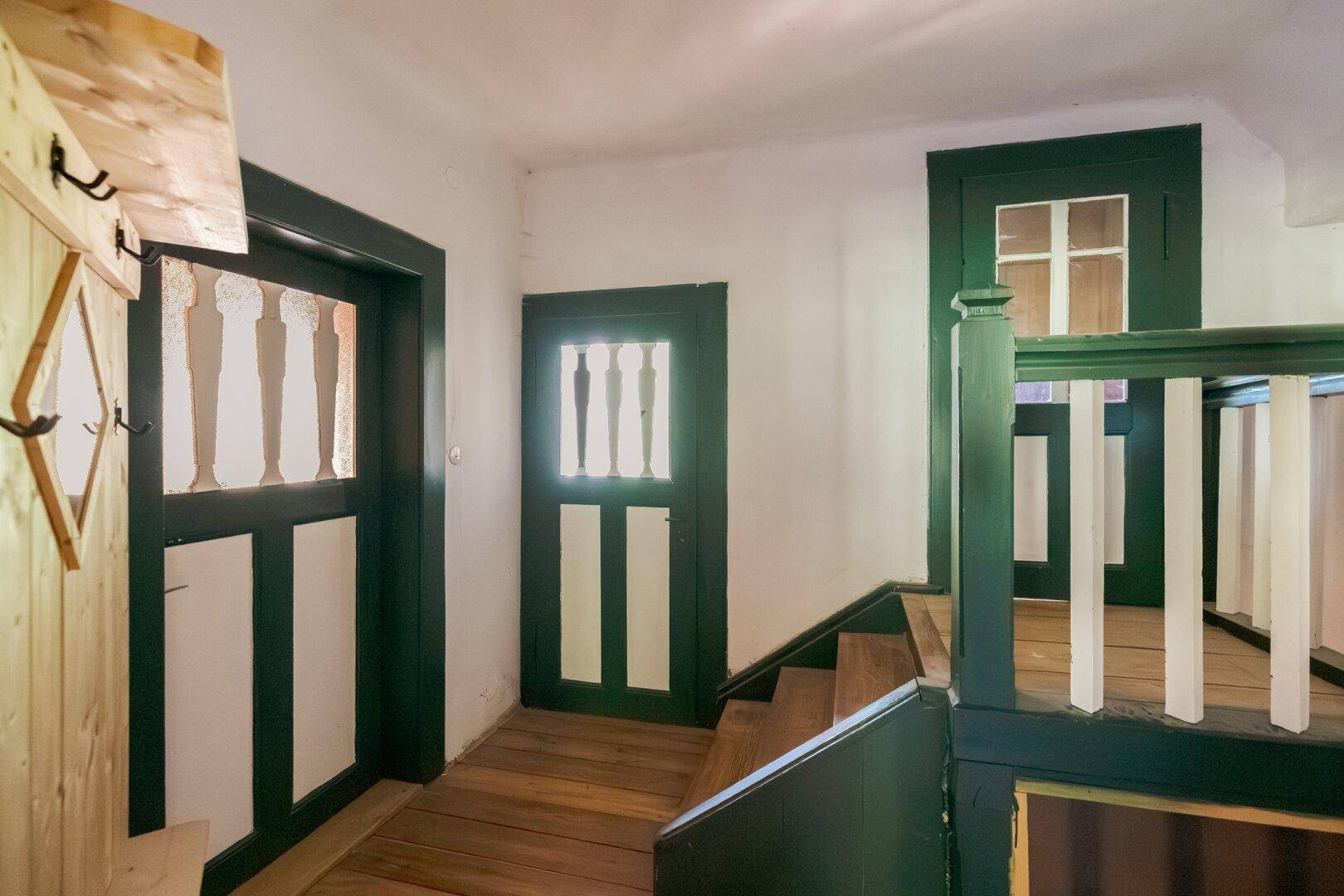Treppenhaus mit traditionellen Holzgeländern und grünen Türen, die den alpinen Stil unterstreichen.