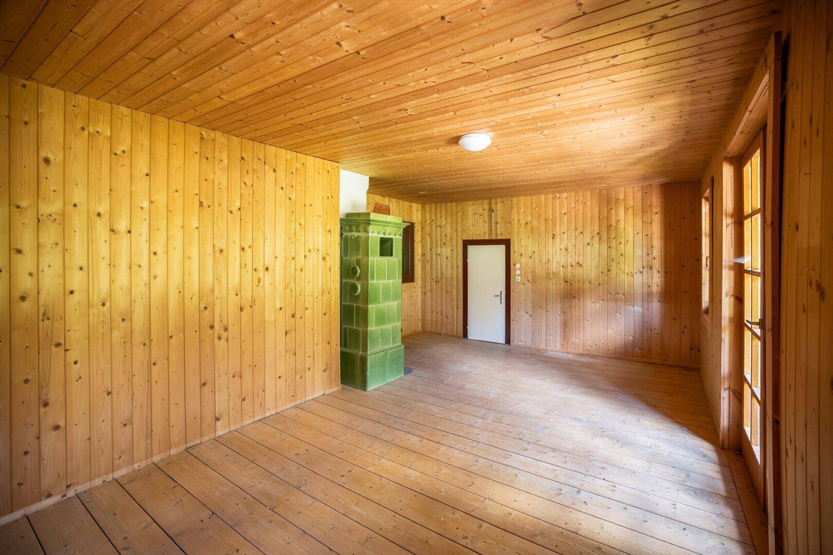 Helles Wohnzimmer mit Holzdielenboden, Holztäfelung und einem traditionellen Kachelofen.