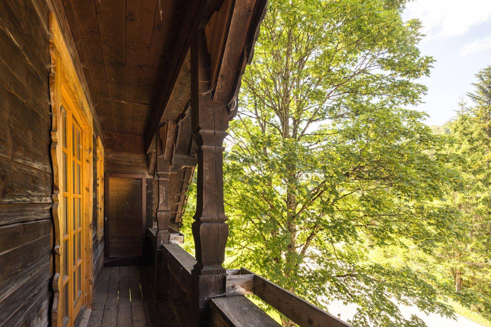 Rustikaler Holzbalkon mit Blick auf die umliegende grüne Landschaft und Bäume.