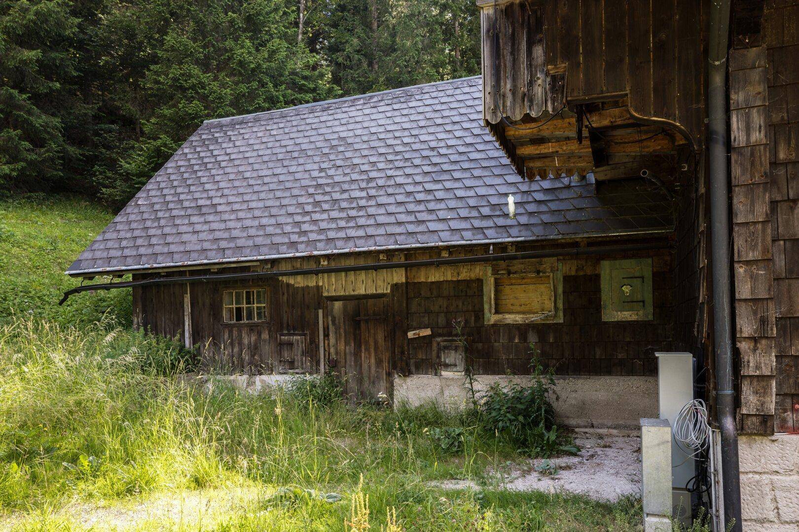 Rückseite des Holzhauses mit Schindeldach und Zugang zu einem Nebengebäude.