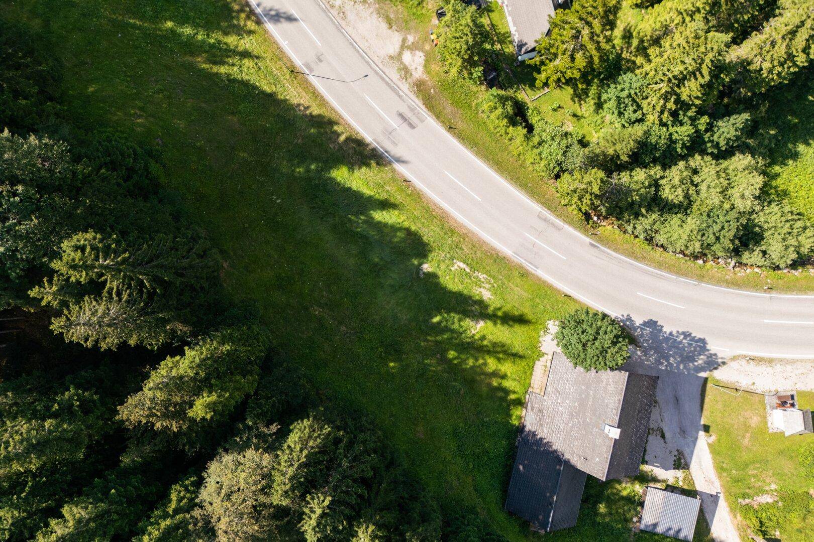 Luftaufnahme des Anwesens mit Haus, Straße und umgebenden Wäldern in alpiner Landschaft.